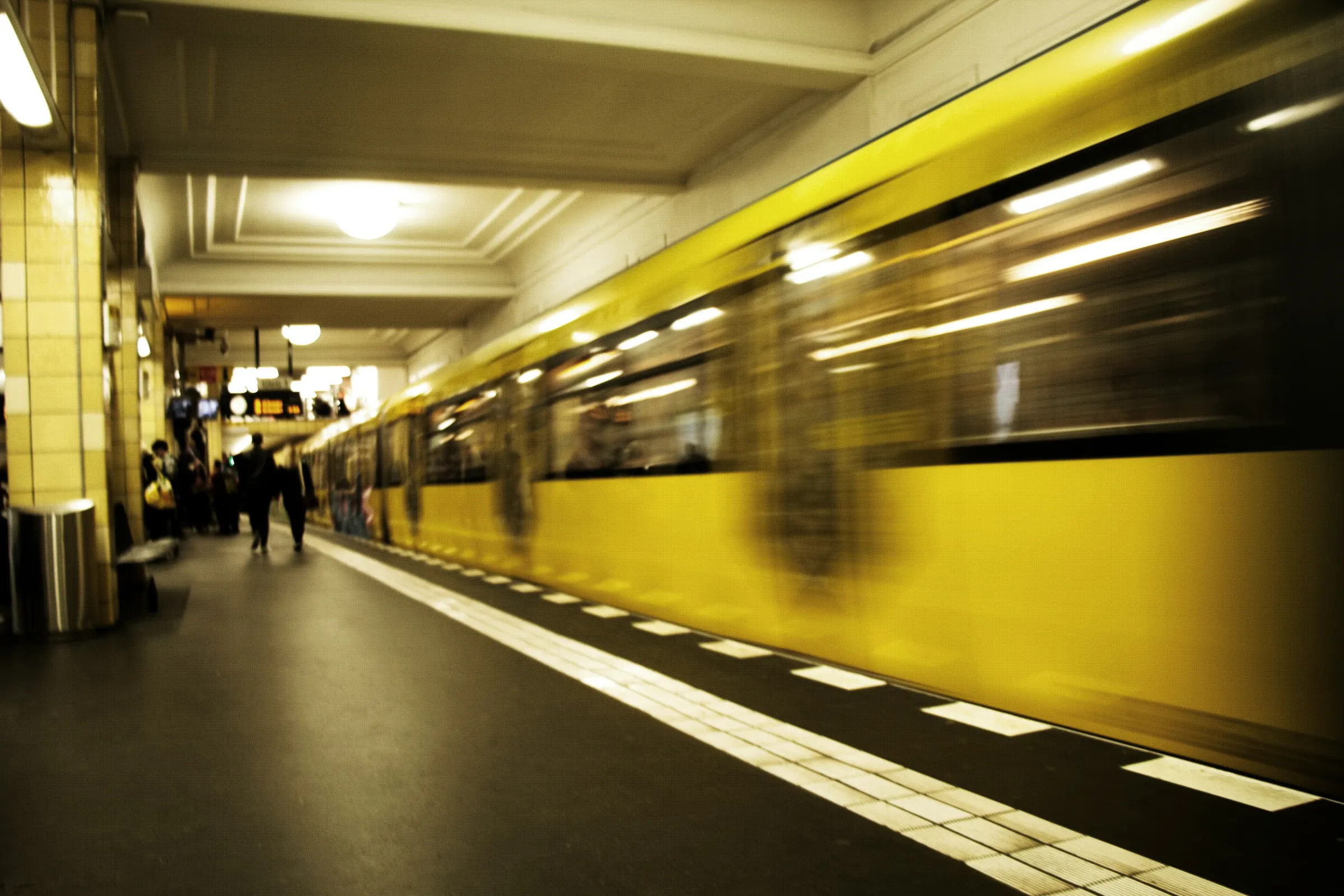 A yellow Berlin U-Bahn train rushing into a station